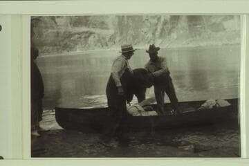 Loading one of Dave Rust's folding canvas boats. Glen Canyon. Bert Loper on the left. Loper on shore and Rust in the boat